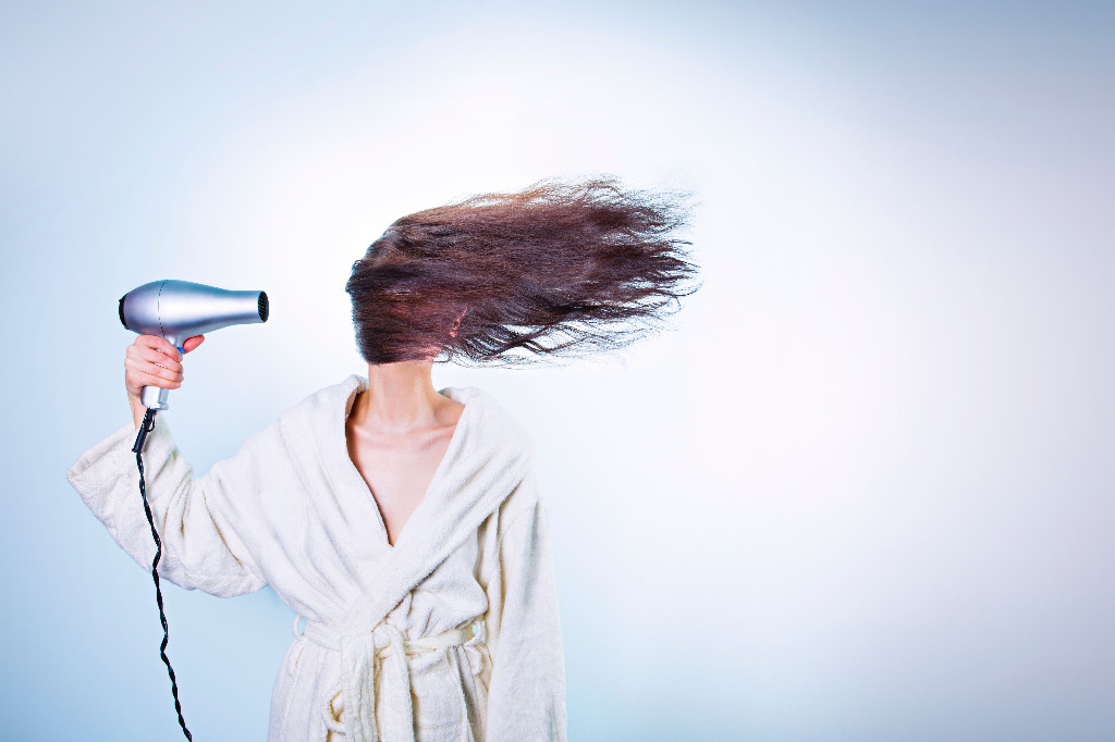 Kobieta w szlafroku susząca włosy suszarką.